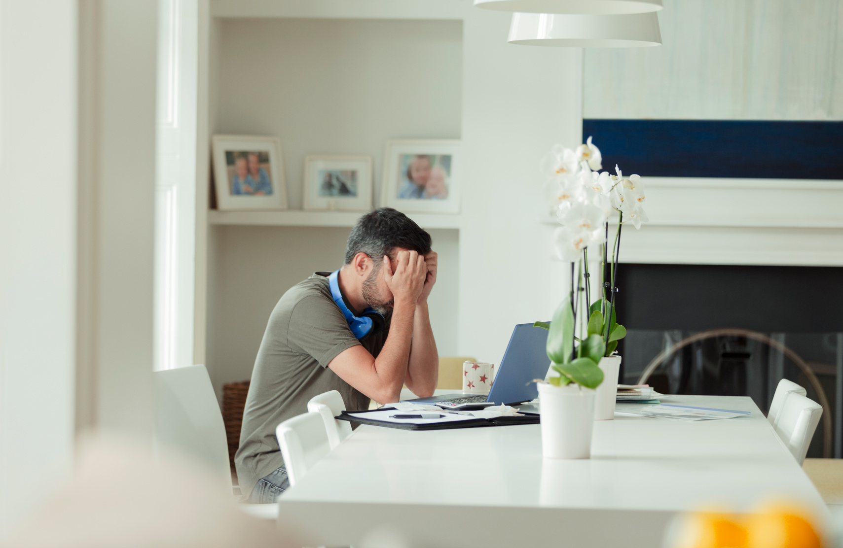 Tired man with head in hands working from home at laptop
