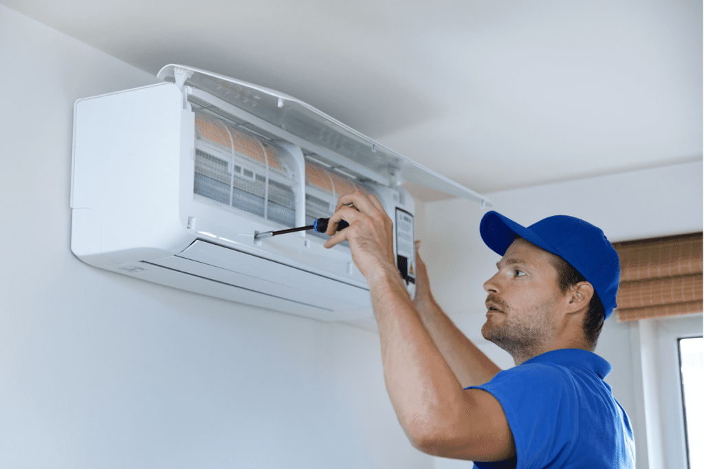 Technician servicing a wall-mounted air conditioning unit in an Australian home, highlighting the importance of spring maintenance and energy-efficient climate control.